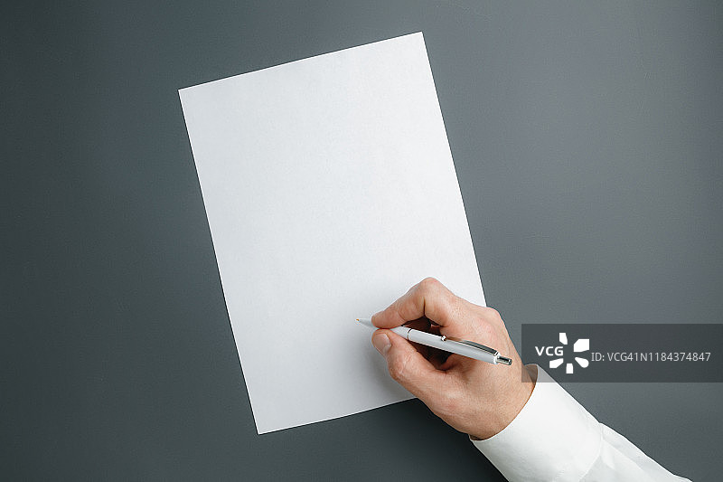 男性手握笔，在灰色背景的空白纸上书写文字或设计图片素材