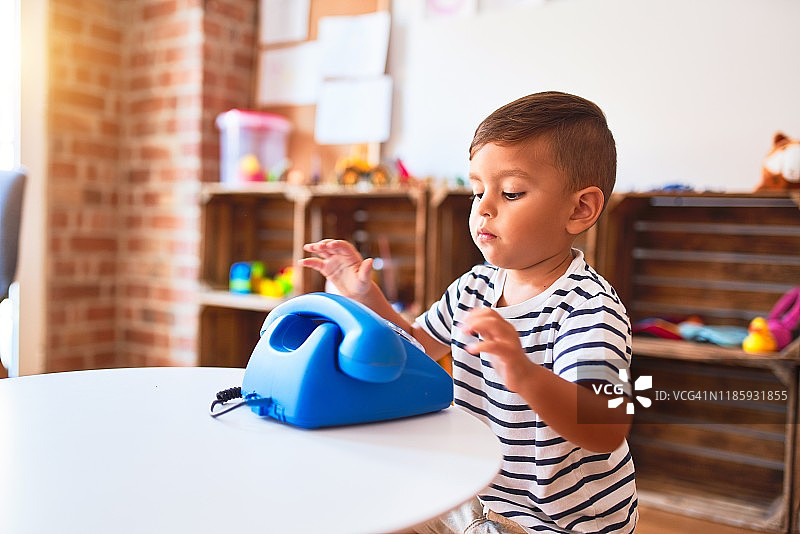 漂亮的蹒跚学步的男孩在幼儿园玩复古的蓝色手机图片素材