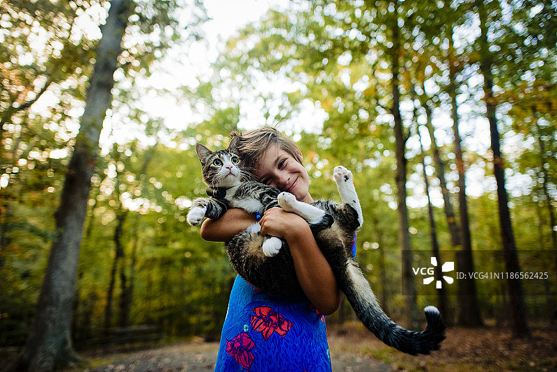 低角度的肖像快乐的女孩抱着猫，而站在森林图片素材