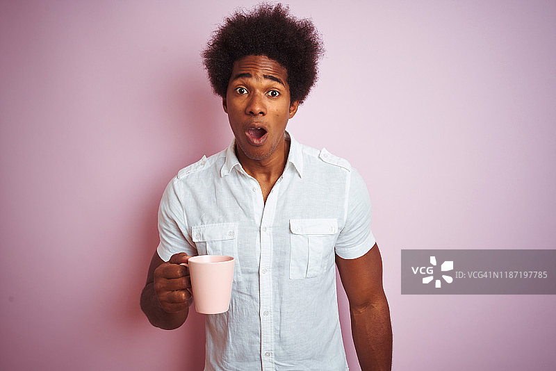 年轻的非洲裔美国人喝一杯咖啡站在孤立的粉红色背景惊吓与惊讶的脸，害怕和兴奋与恐惧的表情图片素材