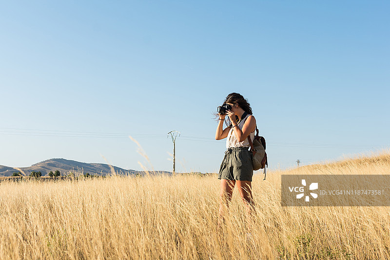 一位年轻女子在阳光下的草地上用相机拍照图片素材