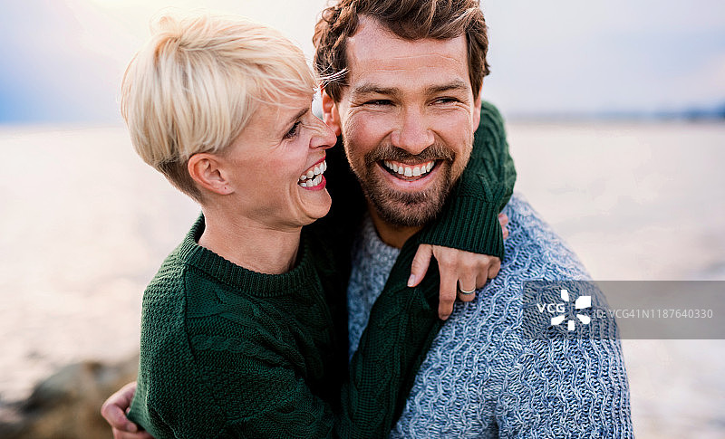 一对快乐的夫妇站在户外的海滩上，拥抱着，大笑着。图片素材