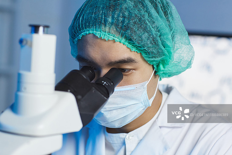 特写年轻的亚洲临床医生在无菌帽和口罩与显微镜工作，同时分析物质图片素材