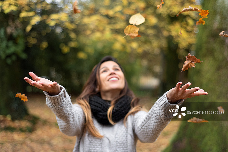 快乐的女人在秋天的公园里扔树叶。图片素材