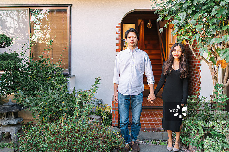 一对年轻夫妇愉快地站在他们的房子前图片素材