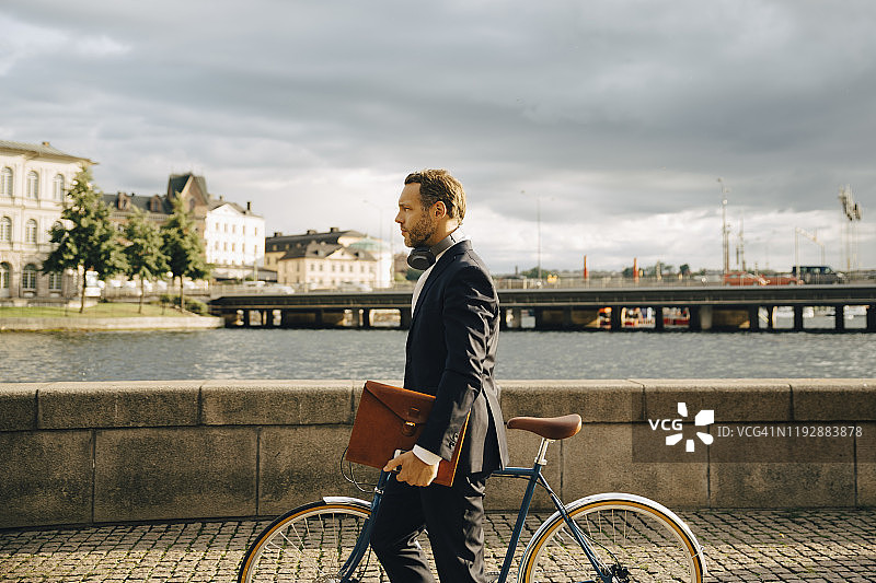 在天空的映衬下，商人在城市的人行道上骑着自行车行走图片素材