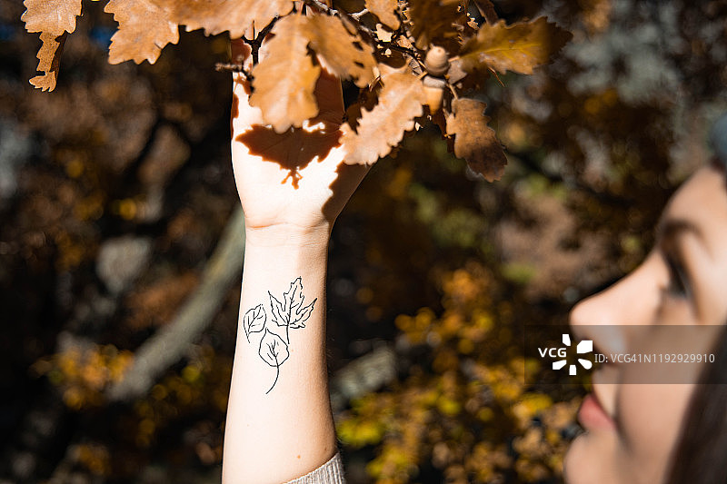 秋天的女人手腕上有叶子纹身。图片素材