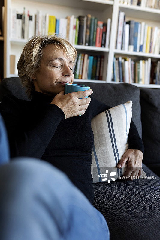 成熟的女人在家里的沙发上放松喝着杯子里的酒图片素材