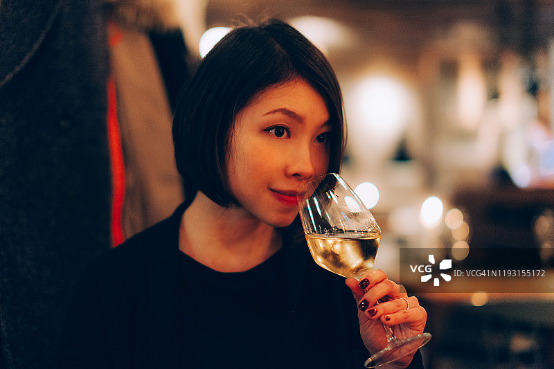 微笑的年轻女子在品尝白葡萄酒的餐厅图片素材