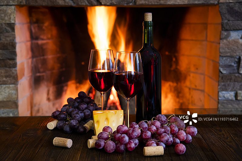 两杯红酒加奶酪和葡萄，放在壁炉旁边图片素材