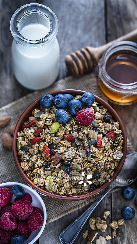 健康早餐:麦片碗，牛奶，蜂蜜和浆果放在木桌上。图片素材