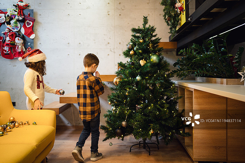 可爱的男孩和女孩在家里装饰圣诞树图片素材
