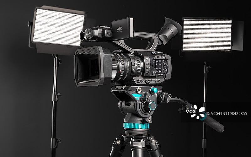 专业4K摄像机在相机三脚架和两个照明LED面板在黑色背景，侧视图图片素材