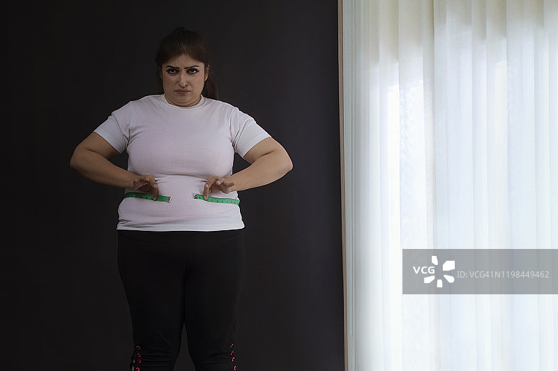 一个超重的妇女在用卷尺量腰围图片素材