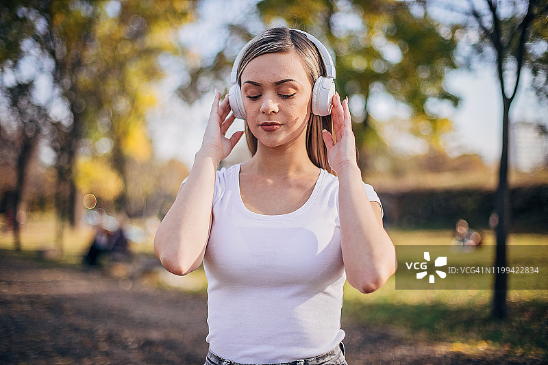 漂亮女人在公园里戴着耳机听音乐图片素材