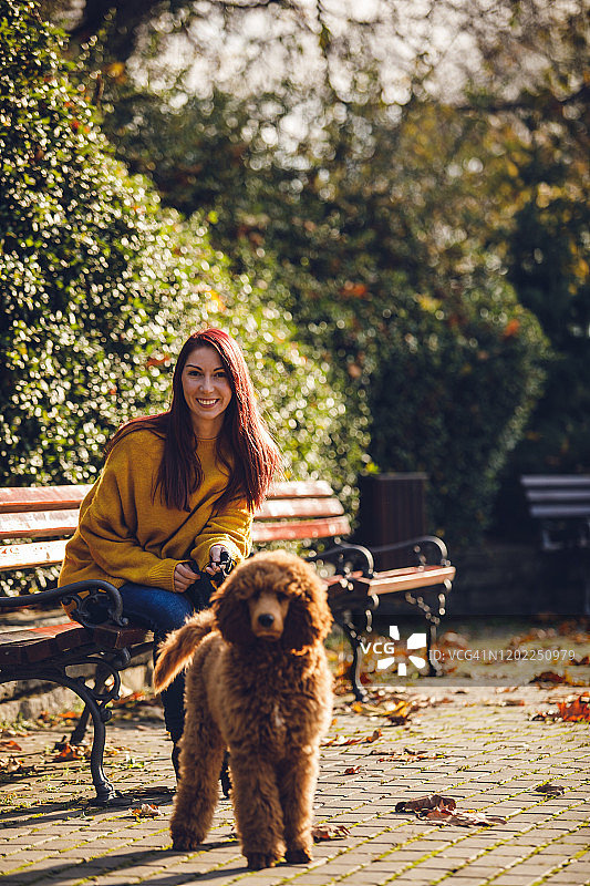 快乐的成年女人和她的宠物坐在公园里图片素材