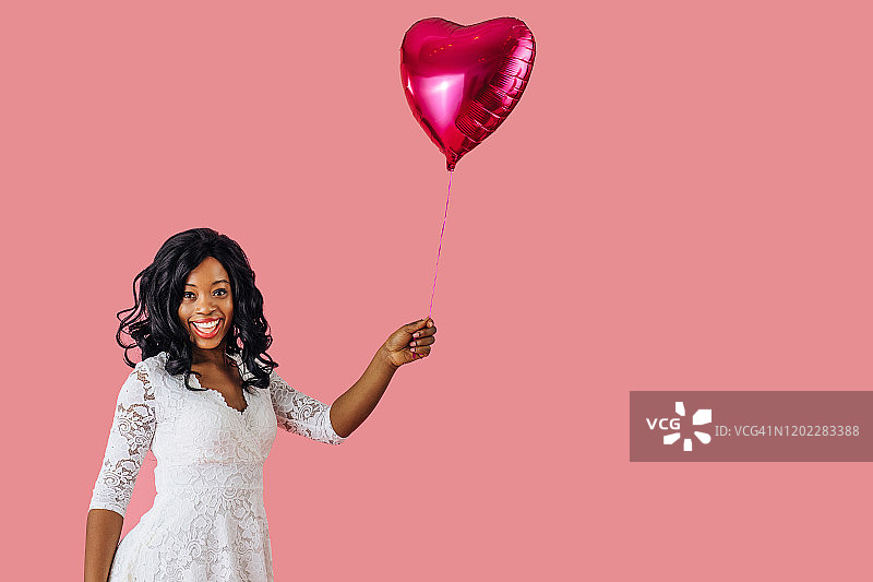 一个年轻快乐的女人拿着粉色的心形气球，情人节坠入爱河的概念图片素材