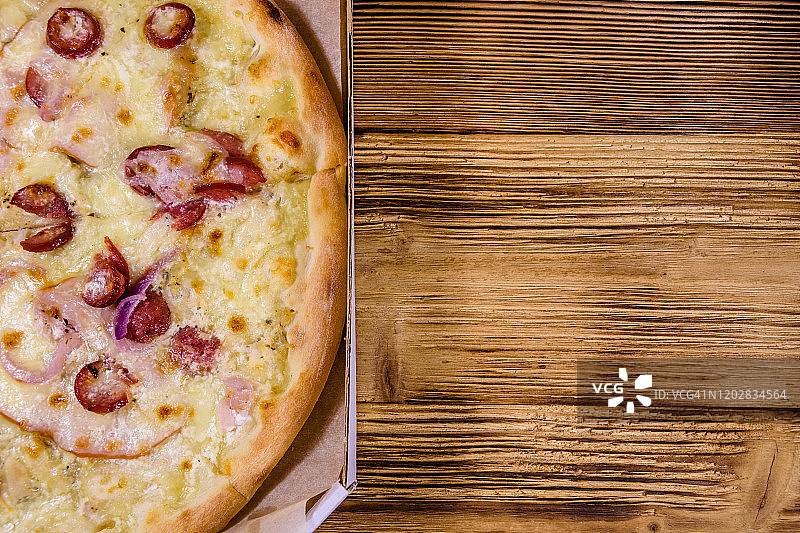 有香肠、火腿和帕尔马干酪的硬纸盒披萨放在木桌上。俯视图图片素材