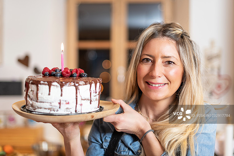在家里烘焙的女人:骄傲地展示她的带浆果的巧克力海绵蛋糕图片素材