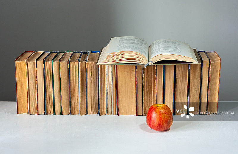 打开精装书，日记，扇形页在一堆书在白色的桌子上与红苹果。书堆积。回到学校的概念。副本的空间。教育学习背景图片素材
