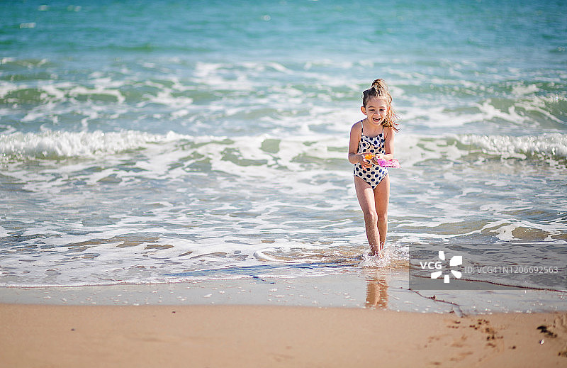 可爱的女孩用粉红色的铲子在沙滩上挖沙子图片素材