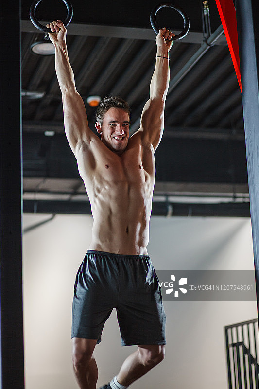 赤裸上身，肌肉发达的男运动员挂在体操吊环上图片素材