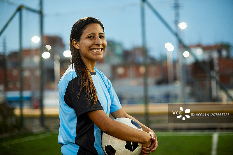 年轻的女足球运动员拿着一个球，看着镜头。图片素材