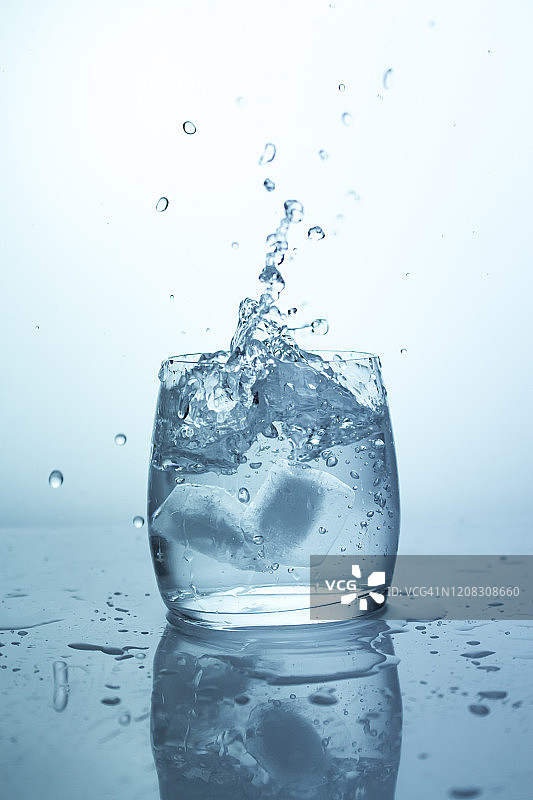 冰落水杯，飞溅的冰块与飞溅，纯净的饮用水在透明的玻璃杯中图片素材