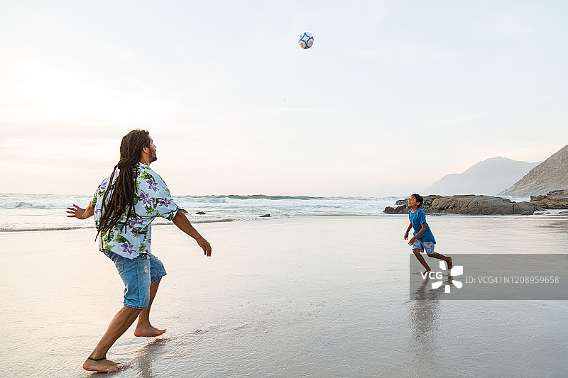 父子俩在沙滩上踢足球图片素材