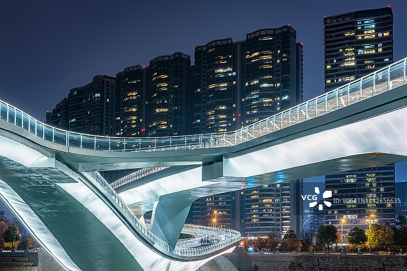 扭曲的现代桥在夜晚被摩天大楼照亮图片素材