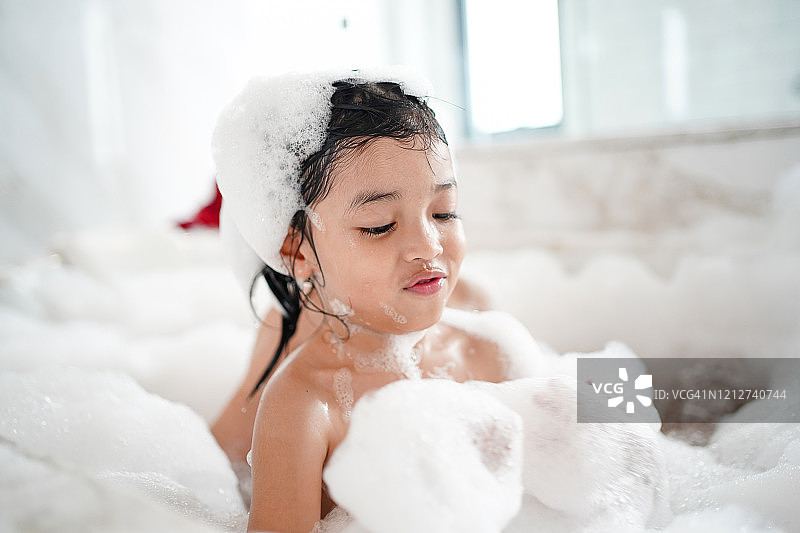 快乐的亚洲小孩洗澡概念。可爱的女孩在浴缸里有蓬松的肥皂泡。图片素材