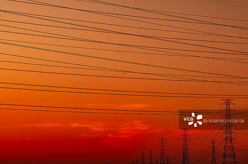 高压塔和电线与日落的天空。电力波兰人。动力和能源支持工厂概念。高压电网塔架带电线电缆。美丽的橙红色日落天空。图片素材