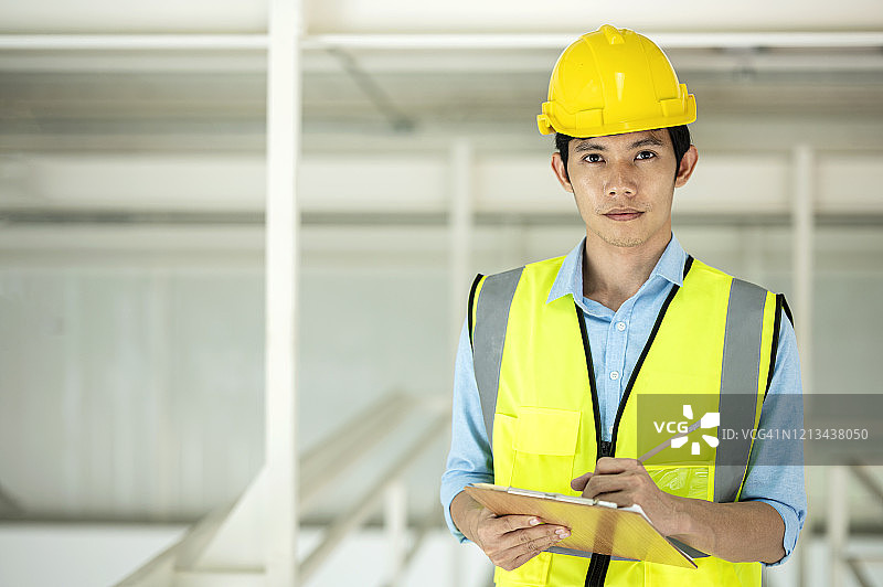 亚洲工厂工程师的肖像穿着安全制服，同时在剪贴板上记录数据。开朗的工程师看着相机在工厂工作。图片素材
