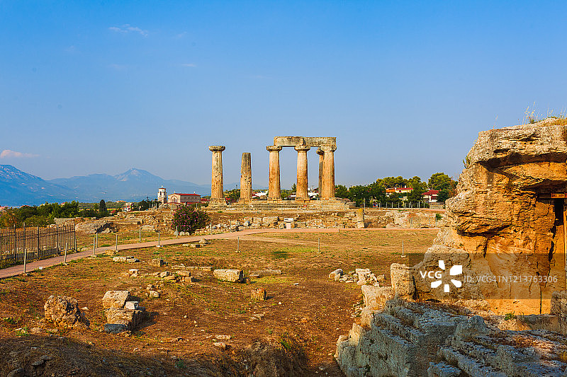 希腊科林斯的阿波罗神庙遗址矗立在一座山冈上，在明亮的阳光下，后面是群山和蓝天图片素材