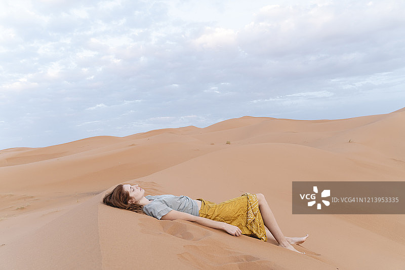 年轻女子躺在撒哈拉沙漠的沙丘，梅尔祖加，摩洛哥图片素材