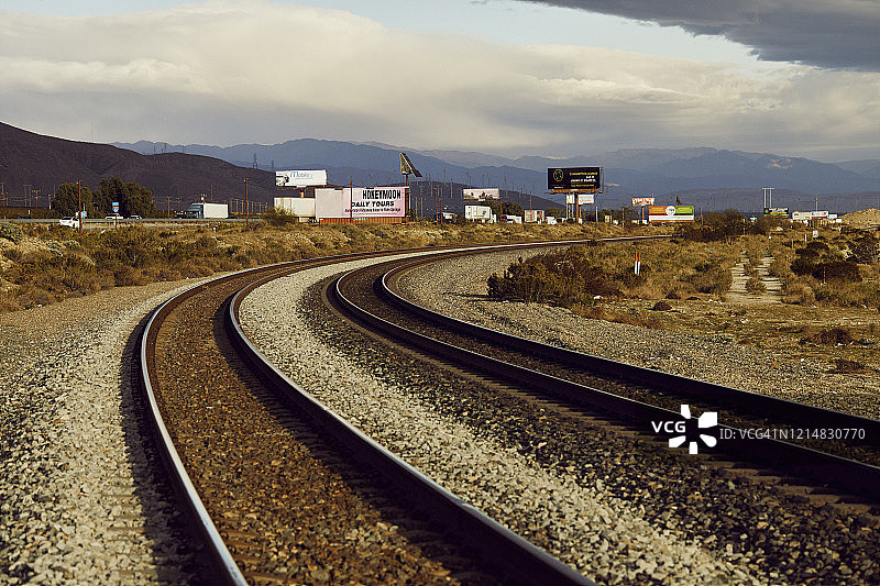 火车轨道在沙漠中弯曲，旁边是繁忙的高速公路和广告牌图片素材