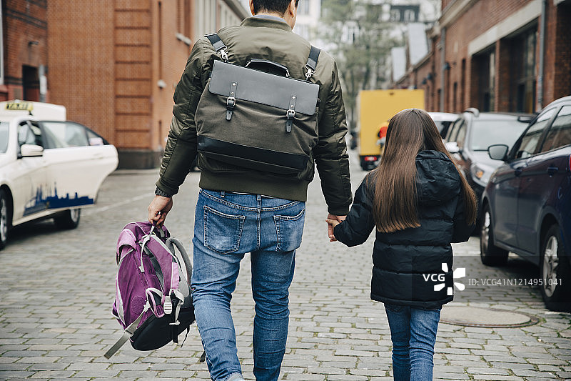 背影的父亲和女儿与背包走在城市的人行道上图片素材