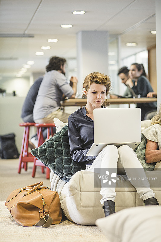 女企业家使用笔记本电脑工作，而其他同事则坐在后面图片素材