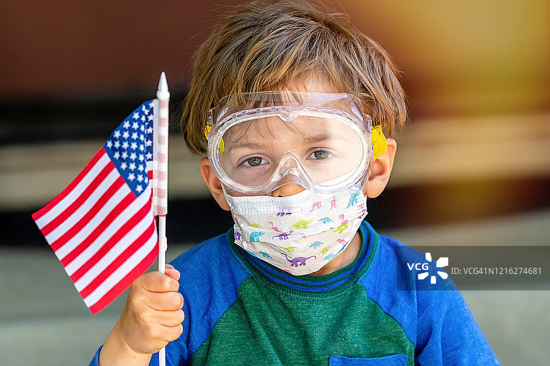 美国白人小男孩摆姿势，戴着防护面具，戴着防护眼镜，举着美国国旗图片素材