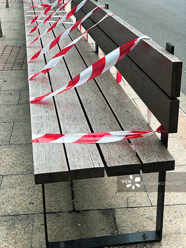 在冠状病毒和COVID-19大流行期间保持社交距离，公共长椅上覆盖着红白屏障和警告胶带图片素材