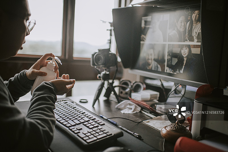 一位亚洲华人男性在他的家庭办公室里做视频/在线博客，用电脑桌面电脑、键盘、鼠标、显示器、蓝牙音箱、带三脚架的单反相机在窗边教授在线摄影课图片素材