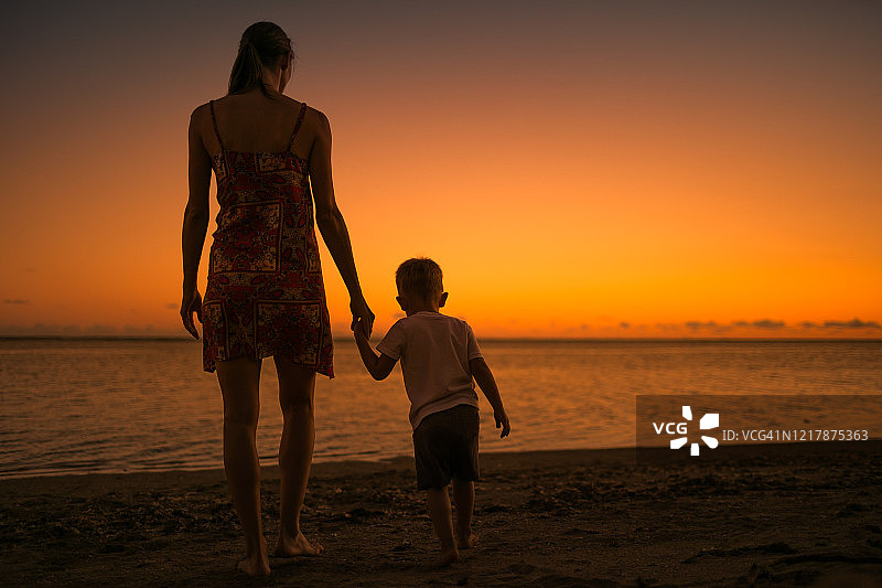 日落时分，母亲和她的孩子手牵着手在海滩公园散步。图片素材