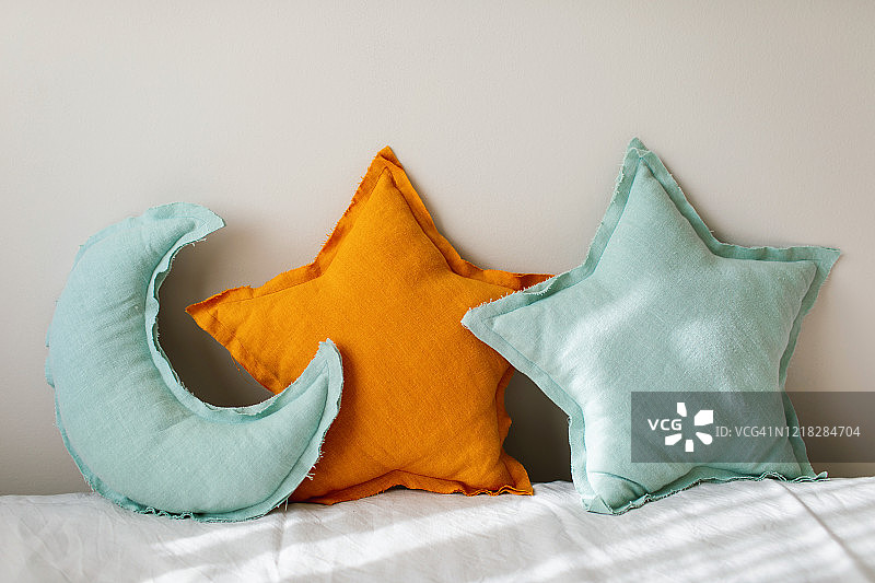 亚麻蓝色和粉红色的月亮和星星枕头玩具在浅米色的背景上轻床上。装饰婴儿坐垫托儿所。图片素材