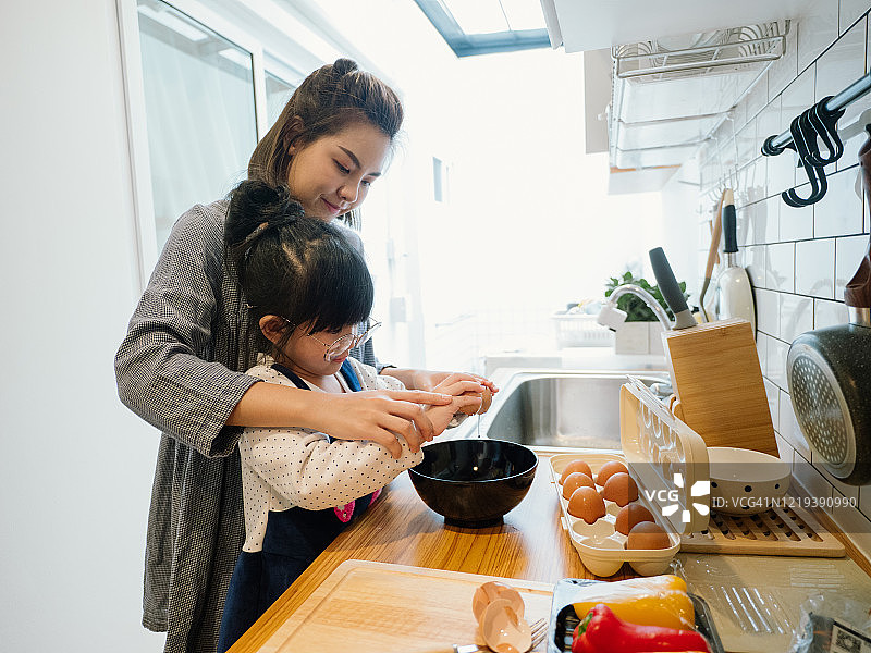 千禧妈妈在厨房准备早餐，而她的女儿在家里帮忙做煎蛋卷。图片素材