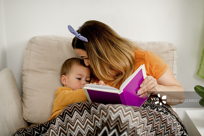 年轻的妈妈在床上给儿子读故事图片素材