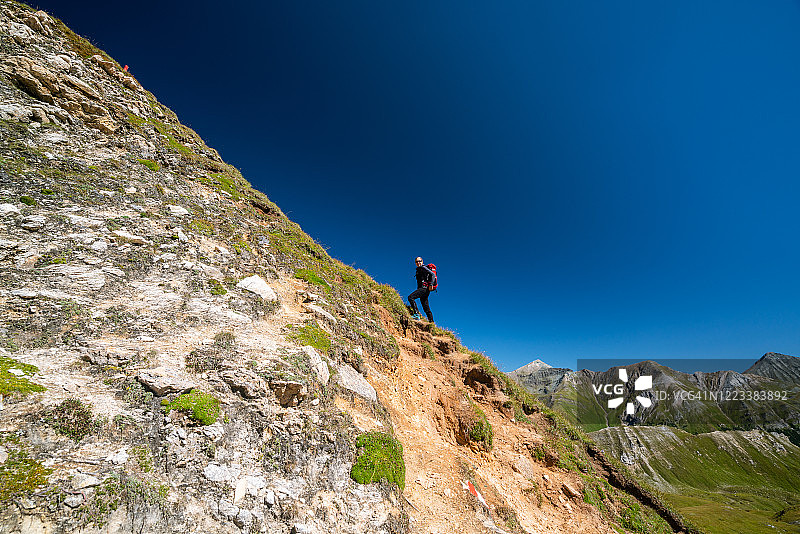 一名妇女正在攀登欧洲阿尔卑斯山脉的陡峭山峰，天空湛蓝图片素材