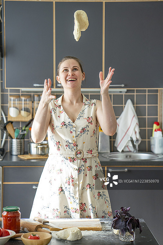 一个快乐的女人在厨房里向空中扔面团的肖像图片素材