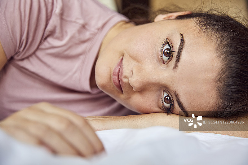 躺在床上的一个年轻女子的肖像，有着棕色的眼睛图片素材