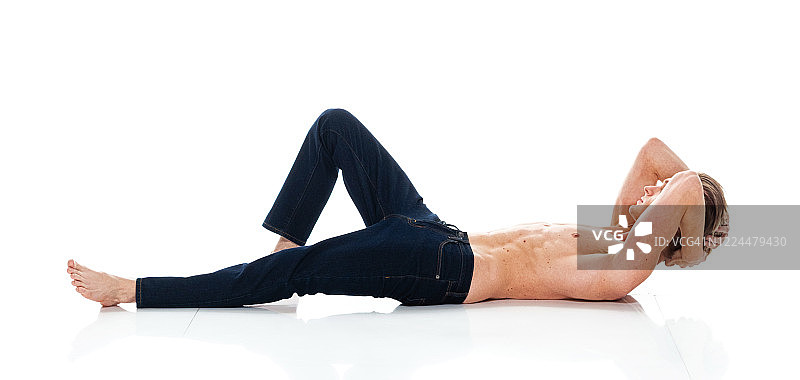 白人年轻男子躺在白色背景下，穿着牛仔裤图片素材