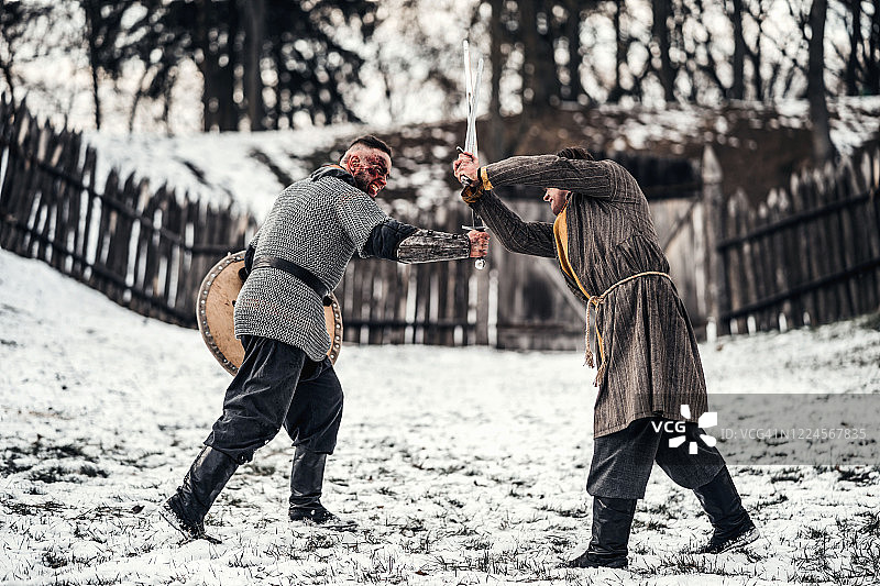 两个身穿盔甲，手持武器的古代战士在雪地里用剑搏斗图片素材